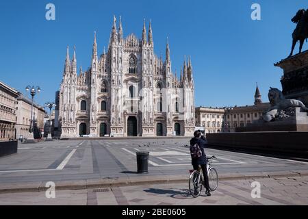 View of deserted Piazza Duomo in Milan, Italy during COVID-19 lockdown with man on bike taking picture. Milano, Italian city and coronavirus pandemic Stock Photo