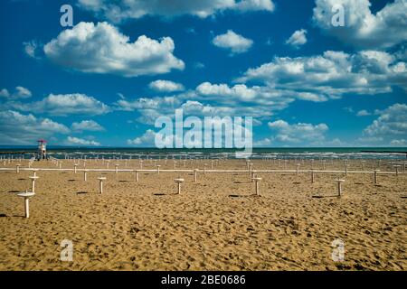 Empty beach of Grado, Italy with lots of Parasol stands and blue sky. Few white clouds, orange sand. Springtime day shot, copyspace Stock Photo