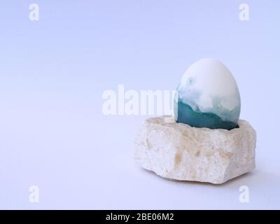 Easter egg isolated colored with a red cabbage natural colour on a white background with blank space on a stone pedestal closeup. Stock Photo