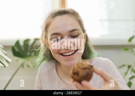 Teenage girl leads culinary vlog for teenagers, girl shows freshly baked chocolate muffin, looks at webcam, tells recipe Stock Photo