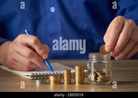 Man calculates the savings. Budget planning concept. Businessman working in the office. Man puts coins into the jar. Stock Photo