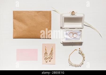 Wedding accessories background. Golden wedding rings and feminine accessories. Golden tinsel, box, earrings, envelope, rings, necklace, bracelet on wh Stock Photo