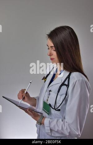 Woman using tablet in healthcare. Lady pharmacist filling out prescription information. Stethoscope over shoulder, isolated on grey background Stock Photo