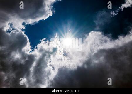 Unusual cloud formations & sunburst against clear cobalt blue sky; central Colorado; USA Stock Photo
