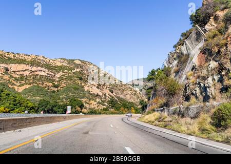 Driving on the scenic Highway 1 through a canyon in Santa Barbara County; metal mesh netting to prevent rock falling due to erosion visible on the rig Stock Photo