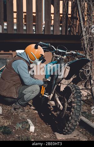 Emoji motocross rider with fancy nerd sunglasses, preparing his motorcycle for a race before season. Emoji with mask protecting against coronavirus Stock Photo