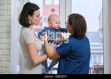 Visit of doctor pediatrician home, mother with baby son of seven months talking with doctor. Examination of child, health and childcare up to one year Stock Photo