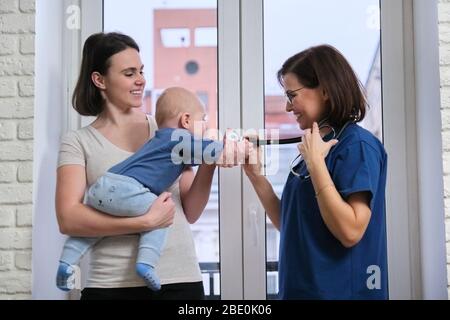 Visit of doctor pediatrician home, mother with baby son of seven months talking with doctor. Examination of child, health and childcare up to one year Stock Photo
