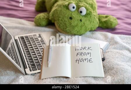 Work from home, text written on notepad. Computer laptop, soft toy and notepad on top of bed in the bedroom. Stock Photo