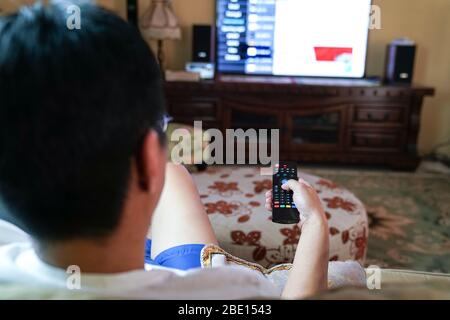 Man watching tv with focus on his hands on the remote control. Home entertainment or stay at home concept. Stock Photo