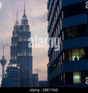 Early evening photo of the Petronas Towers with an office building and silhouetted worker in the foreground in Kuala Lumpur, Malaysia. Stock Photo