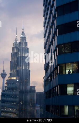 Early evening photo of the Petronas Towers with an office building and silhouetted worker in the foreground in Kuala Lumpur, Malaysia. Stock Photo