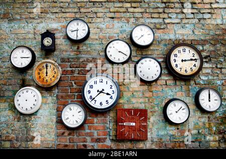 A lot of vintage clocks of different sizes hanging on a grunge brick wall. Round and square clocks show different time. Some have no hands. Stock Photo