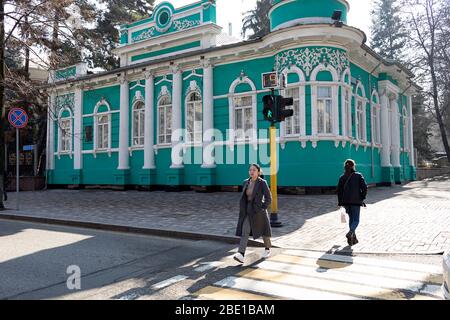 Pedestrians crossing street on green traffic light at old merchant's trade house with stucco floral ornaments, street scene in Almaty, Kazakhstan Stock Photo