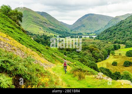 Mountain biker climbing towards Boredale Hause in the Lake District. Brothers Water, Caudale Moor, Kirkstone Pass and Red Screes behind.