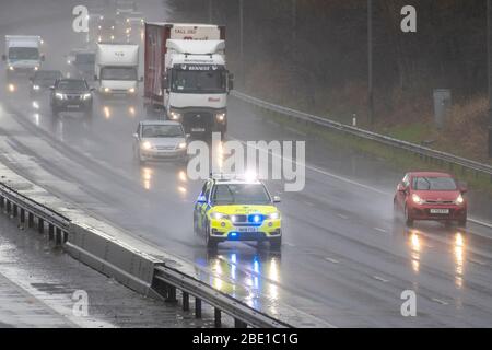 Police blue lights car on 999 call emegerncy response on the M6 during heavy rain shower in Chorley, Lancashire. Heavy rain, hail showers, poor visibility and wintery February wet weather make for very difficult driving conditions with slippery surfaces for motorists travelling on the the M6 motorway. Stock Photo