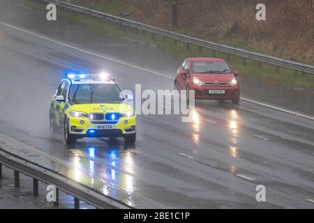 Police blue lights car on 999 call emegerncy response on the M6 during heavy rain shower in Chorley, Lancashire. Heavy rain, hail showers, poor visibility and wintery February wet weather make for very difficult driving conditions with slippery surfaces for motorists travelling on the the M6 motorway. Stock Photo