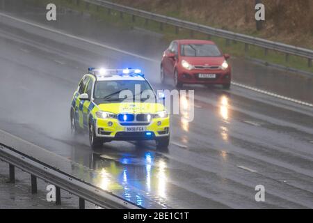 Police blue lights car on 999 call emegerncy response on the M6 during heavy rain shower in Chorley, Lancashire. Heavy rain, hail showers, poor visibility and wintery February wet weather make for very difficult driving conditions with slippery surfaces for motorists travelling on the the M6 motorway. Stock Photo