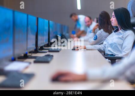 Group of Security data center operators (administrators) working in a group at a CCTV monitoring room while looking at multiple monitors ( computer sc Stock Photo