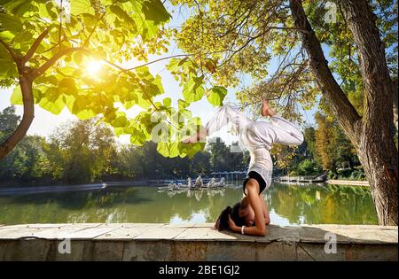 Beautiful Asian girl in white costume doing head stand yoga position in the park Stock Photo