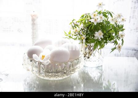 Spring flowers in a glass and white eggs in a crystal vase on a white background. Stock Photo