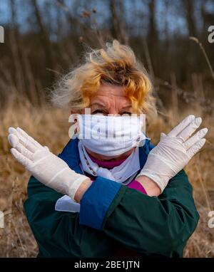 An elderly woman in a medical protective mask and rubber gloves gestures stop coronavirus.  Stock Photo
