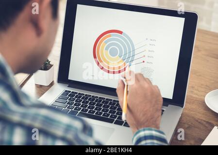 Asian man analyzing and working with financial business diagram on laptop computer at home Stock Photo
