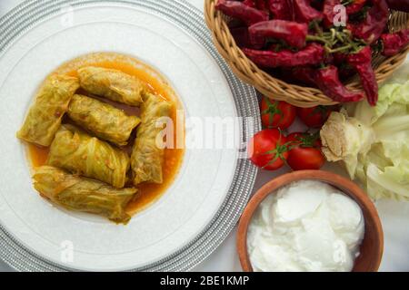 Meat stuffed cabbage leaves, stewed in tomato sauce . Cabbage stuffing on a white plate . Red pepper in the basket. Red tomatoes and cabbage. Yogurt Stock Photo