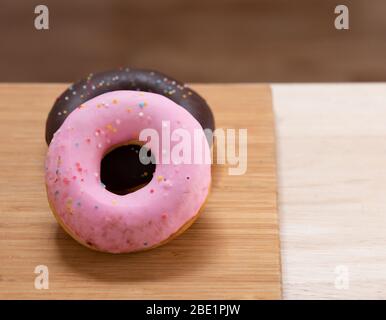 Two donuts are pink, Chocolate with sprinkles isolated on wood background. Stock Photo