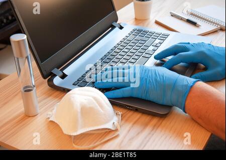 Male hands in blue protective gloves working on modern laptop. Specialist doctor in blue latex gloves. Medical mask and test tube vaccine are on the d Stock Photo