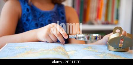 Little girl looking the world map with a magnifying glass and a compass. Planning a trip. Discovery of the world through books and maps. Travel concep Stock Photo