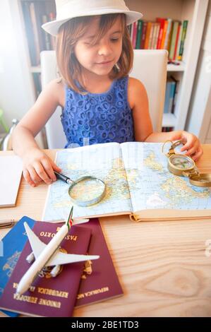 Trendy little girl in summer casual wear and white hat, looking the world map with magnifying glass and compass. Planning a trip with family. Passport