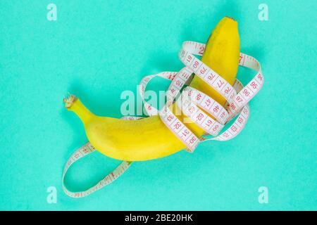 Banana with tape for measuring figure. Centimeter ruler spinned around fruit. Tape wrapped around banana isolated on mint background. Weight loss Stock Photo