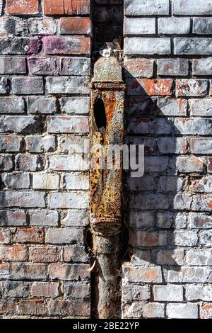 Rusty old drain pipe and red brick wall of dilapidated building Stock Photo