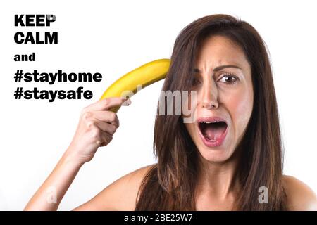 Portrait of a beautiful girl trying to shoot herself with a banana gun, while screaming. With message for COVID-19 alarm, Coronavirus, quarantine and Stock Photo