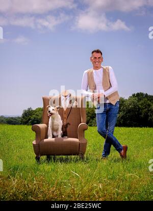Furniture designer Shaun Brownell of Rhubarb Chairs photographed with one of his suit armchairs and his dog Bambam near his Sussex studio, UK Stock Photo