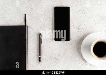 Up-to-date smartphone with notebook, fountain pen and cup of coffee on concrete background. Workstation concept flat lay. Coffee break top view. Mocku Stock Photo