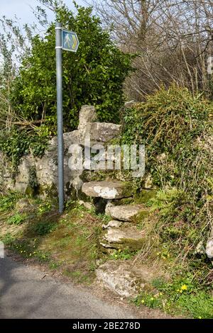 Footpath signpost by quaint old stone stile steps over a wall on a country lane near Benllech, Isle of Anglesey, Wales, UK, Britain Stock Photo