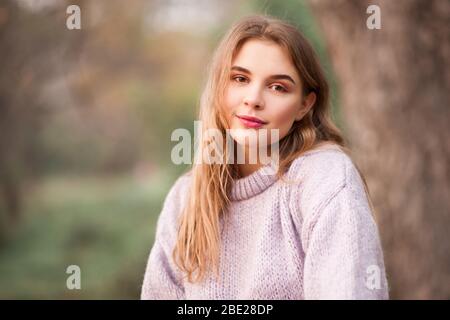 Beautiful blonde teen girl 16-18 year old wearing knitted sweater posing outdoors over nature background. Looking at camera. Spring season. Stock Photo