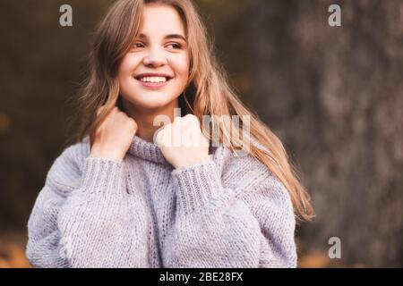 Smiling teen girl 16-17 year old wearing knitted sweater posing outdoors closeup. Fashionable. Autumn season. Stock Photo