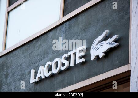 Lacoste brand white text on black wall. There is a crocodile mark on the side. Stock Photo