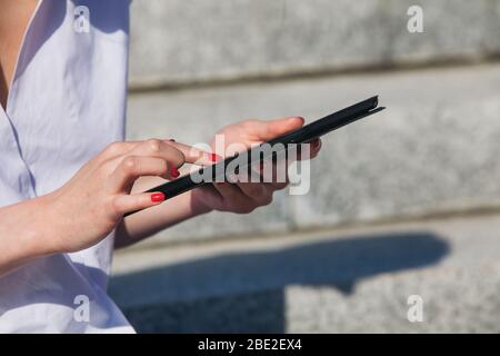 Woman is sitting on the steps in city in sunny day and uses e-book Stock Photo