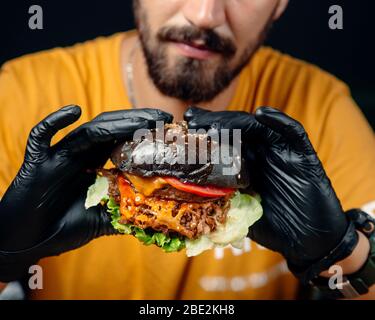 guy in black gloves holds a juicy cheeseburger in brown bread Stock Photo