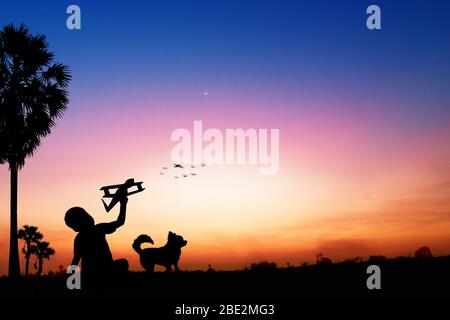 Silhouette of kid dreams as pilot sitting and holding airplane paper with friend running with wind turbine in sunset, imagination and freedom  idea co Stock Photo