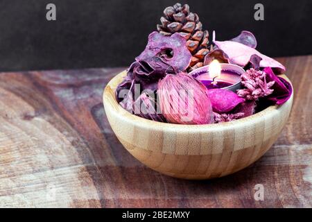 pourple tealight and dry potpourri in a wooden bowl over a table with black background Stock Photo