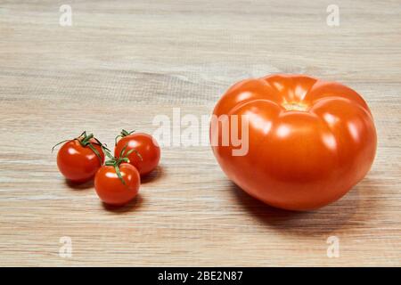 three small cherry tomatoes next to a large ordinary tomato on the table Stock Photo