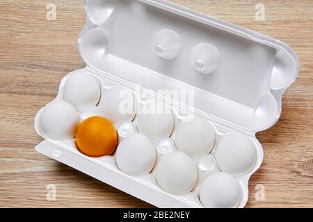 nine white eggs and one golden yellow are packed together in one egg crate on a wooden table surface Stock Photo