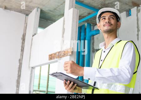 Inspector holding clipboard opening paper and checking building for renovation, engineer surveyor looking in construction site Stock Photo