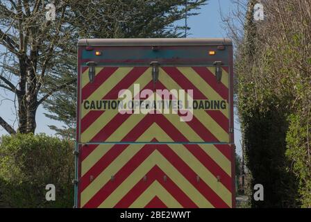 'Caution Operatives Loading' Sign on the Back of a Recycling Truck on a Narrow Country Lane in a Village in Rural Devon, England, UK Stock Photo
