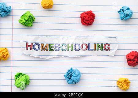 The word Homeschooling written on a lined notebook sheet with some crumpled paper balls around it. Close up. Stock Photo